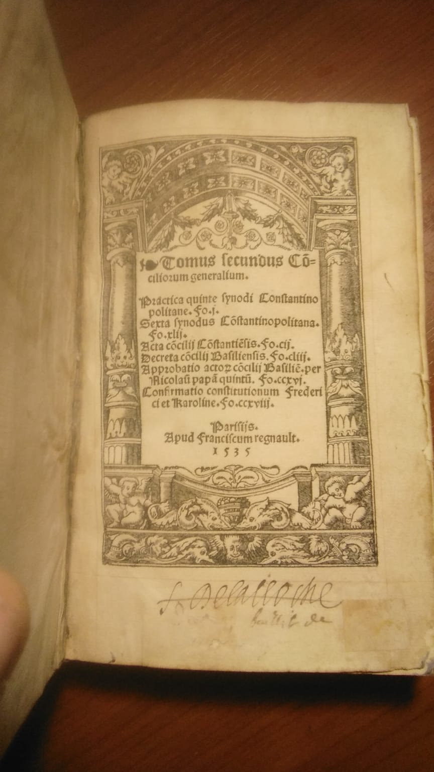 The woodcut title page, printed in Gothic black letter within a full-page architectural border of classical columns, a coffered arch, putti, grotesque masks and dolphins. The imprint below reads Parisiis, apud Franciscum Regnault, 1535, and an early manuscript ownership inscription in brown ink runs across the foot of the leaf.