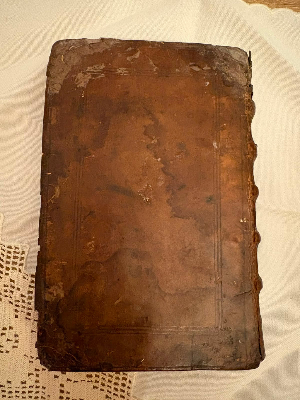A board of the binding photographed flat, showing the blind-tooled triple-fillet panel, heavy staining and darkening across the calf, and surface loss and wear at the corners and along the edges.