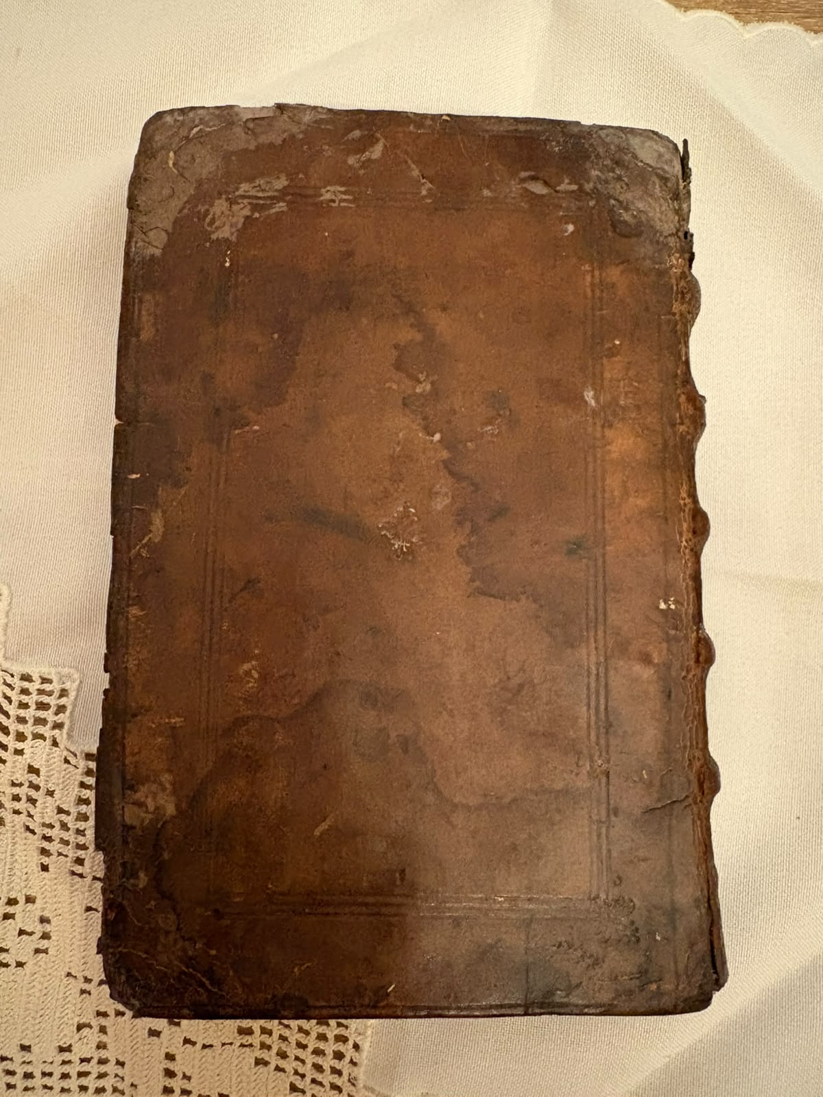A board of the binding photographed flat, showing the blind-tooled triple-fillet panel, heavy staining and darkening across the calf, and surface loss and wear at the corners and along the edges.